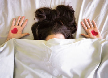 Close-up of woman under blanket with heart shape drawn on hands