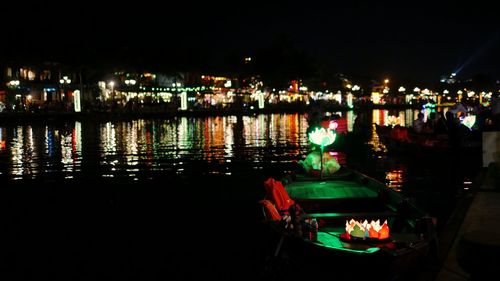 Boats in river against illuminated city at night