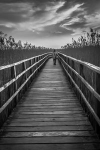 Rear view of woman walking on footbridge against sky