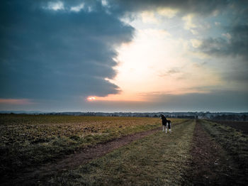 People walking on field against sky during sunset