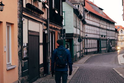 Rear view of man walking on street amidst buildings in city