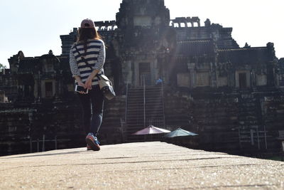 Rear view of woman on wall walking towards old ruin