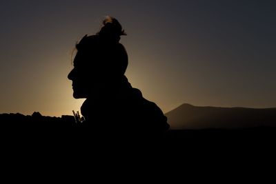 Silhouette man on rock against sky during sunset