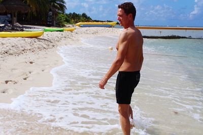 Side view of shirtless man standing on beach