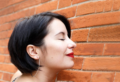 Close-up portrait of a young woman against brick wall