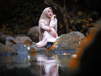 Woman standing by rock with reflection in lake