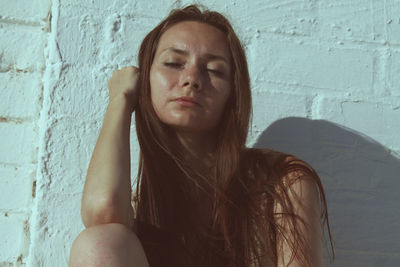 Portrait of a beautiful young woman sitting against wall