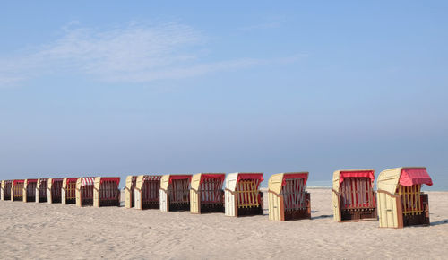 Hooded chairs on beach against sky