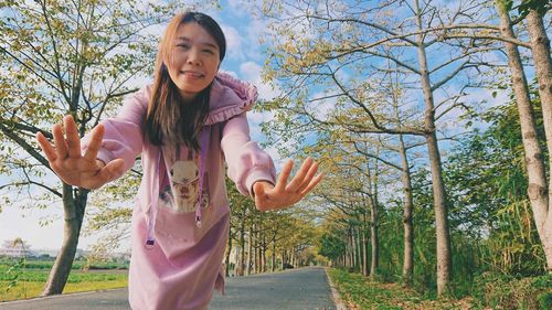 Portrait of woman gesturing while standing against trees