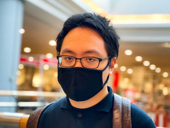 Portrait of young man wearing eyeglasses and face mask against neon lights inside mall.