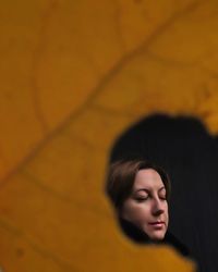 Close-up of woman with eyes closed seen through hole in leaf