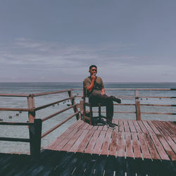 Man sitting on seat by sea against sky