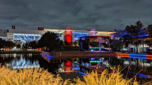 Illuminated city by lake against sky at night