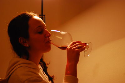 Young woman drinking wine while standing against wall at home