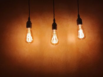 Low angle view of illuminated light bulb hanging from ceiling