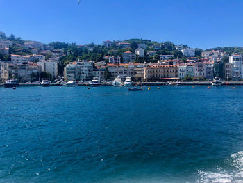 Sailboats in sea by town against clear blue sky