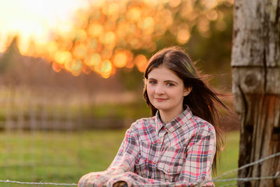 Portrait of young woman standing outdoors by barbed wire fence