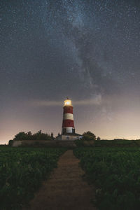 Lighthouse amidst field against sky at night