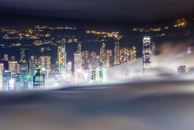 Illuminated cityscape covered with clouds at night