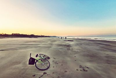 Bicycle on beach against sky during sunset
