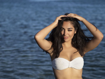 Portrait of young woman in bikini standing at beach