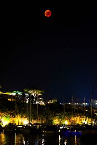 Illuminated ferris wheel at harbor against clear sky at night