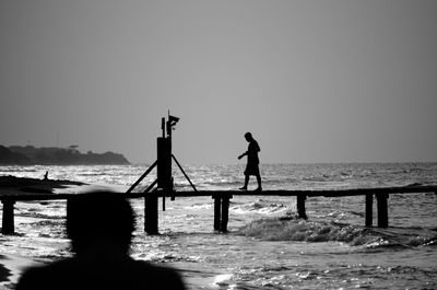 Silhouette man walking on pier over sea against clear sky