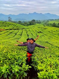 Portrait of friends with arms outstretched standing amidst plants on field