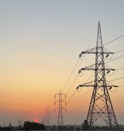 Low angle view of electricity pylon against sky during sunset