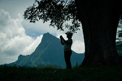 Man standing by tree trunk against sky