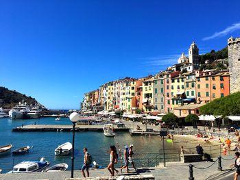 Boats moored on sea by city against clear blue sky