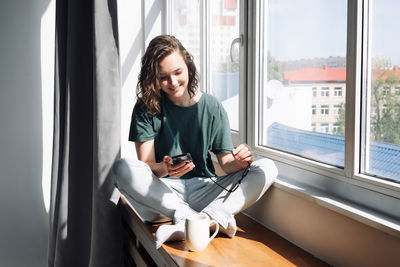 Portrait of young woman sitting on window