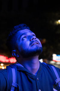 Close-up of young man looking up by illuminated lights