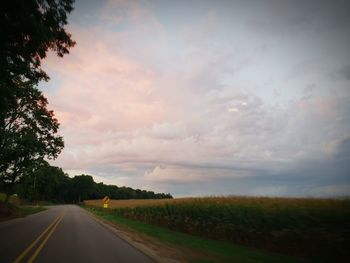 Road by trees against sky during sunset