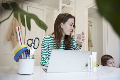 Blogger with laptop drinking water while looking at daughter