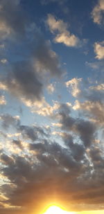 Low angle view of sunlight streaming through clouds during sunset