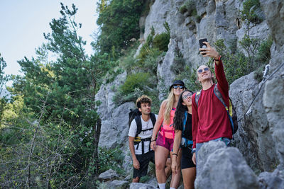 Group of friendly tourists with backpacks standing in highland area and taking photo on selfie camera during vacation