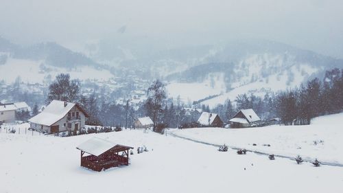 Snow covered landscape and houses against mountains during winter
