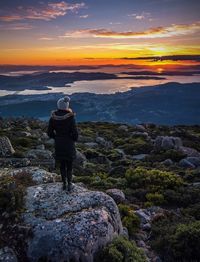 Rear view of man standing on rock against sky during sunset