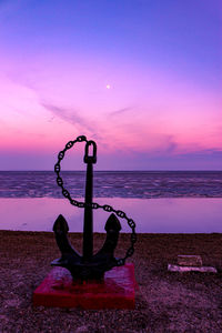 Fire hydrant on sea against sky during sunset