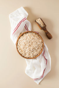 Oat flakes in a wooden bowl on a napkin on a beige background.