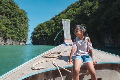 Full length of woman sitting on riverbank against trees