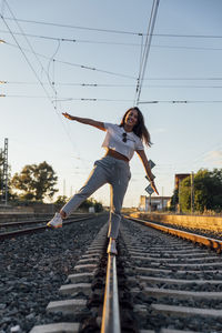 Full length of young woman on railroad tracks against sky