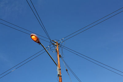 Low angle view of overhead cable cars against clear blue sky