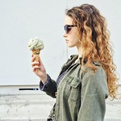 Young woman looking at ice cream while standing against wall