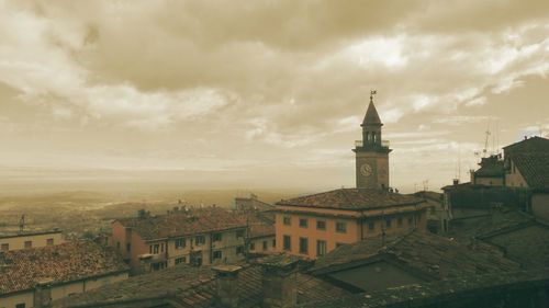 Church tower in town against cloudy sky