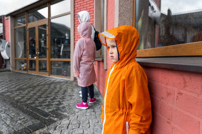 Boy wearing raincoat while standing by wall