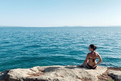 Full length of shirtless man sitting on sea against sky