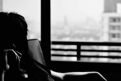 Rear view of woman sitting on window