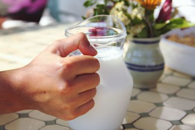 Cropped image of hand holding milk in jug on table